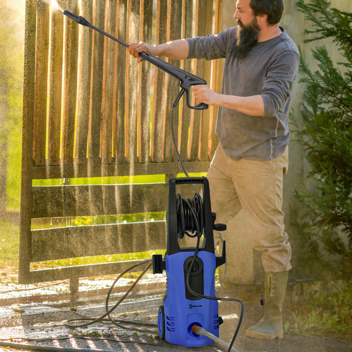 Man using a pressure washer to clean a wooden fence outdoors.